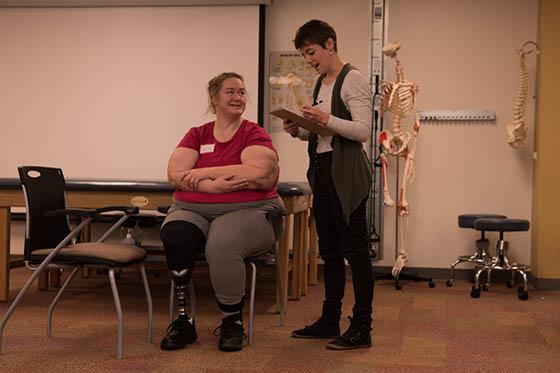 图为波胆网站的一名学生看着剪贴板，帮助一位坐着的病人, 谁戴了假肢