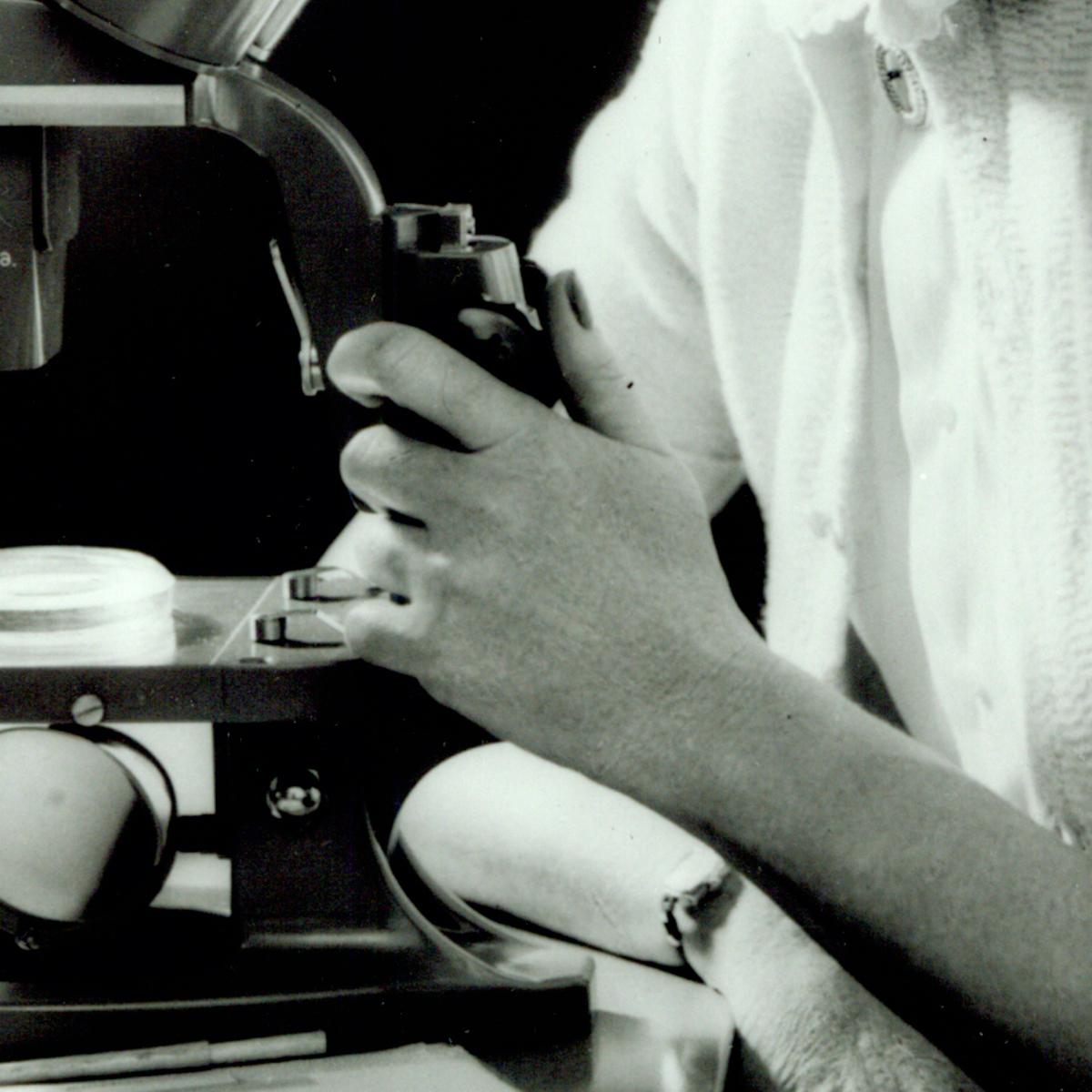 Close-up black and white photo of Rachel Caron's hands operating a microscope
