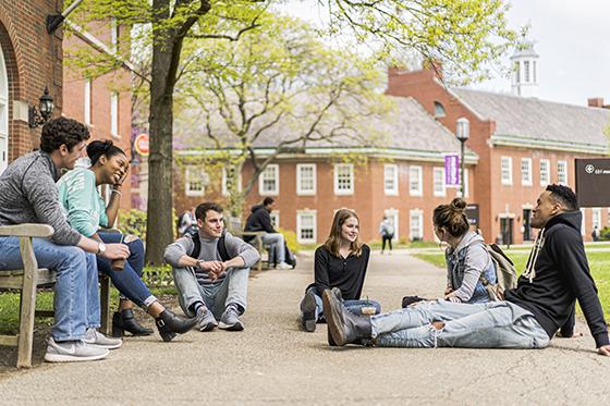 图为六名波胆网站学生坐在红砖教学楼外的地上和长椅上聊天